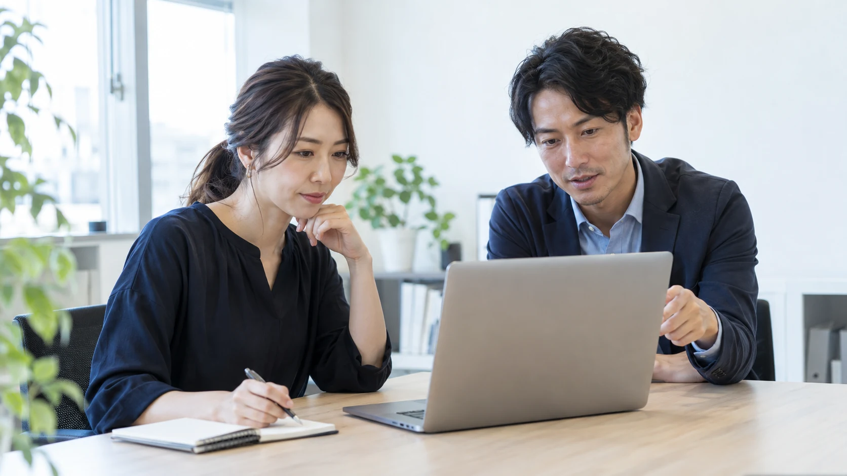 明るいオフィスでノートパソコンを見ながら顧客の情報収集について話し合う担当者たち（AI生成イメージ）